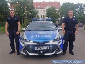 Policjanci z komisariatu policji Wrocław-Grabiszynek w umundurowaniu stojący przy radiowozie oznakowanym
