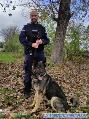 Zdjęcie ilustracyjne umundurowanego policjanta wraz z psem służbowym