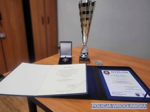 Stojące na stole puchar, medal oraz dyplom i inne dokumenty gratulacyjne