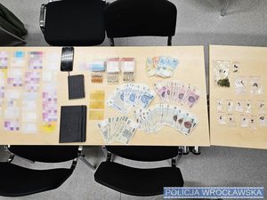 Leżące na stole karty płatnicze, SIM, narkotyki w woreczkach foliowych oraz banknoty polskich złotych oraz euro o różnym nominale oraz notesy