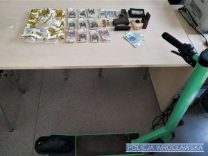 Przedmioty ujawnione przy zatrzymanym leżące na biurku, obok stoi hulajnoga elektryczna koloru zielonego