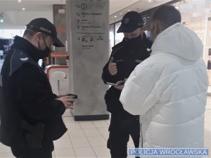 Policjanci legitymujący mężczyznę w białej kurtce