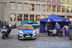 Zdjęcie przedstawia policyjne stoisko profilaktyczne na wrocławskim rynku