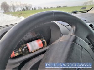 Zdjęcie przedstawia wnętrze pojazdu oraz butelkę alkoholu