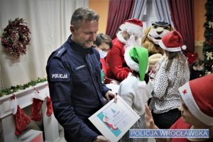Dzieci wręczają podziękowania. Od lewej: policjant, przedstawicielka centrum handlowego, Święty Mikołaj oraz Komisarz Lew