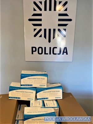 Kartonowe pudełka z maseczkami ochornnymi na tle plakatu z gwiazdą policyjną