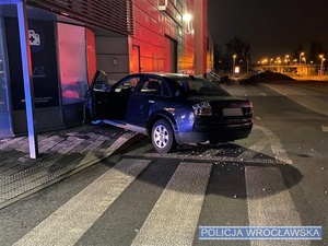 Osobowy samochód marki audi stojący, w nocy, z rozbitym przodem w witrynie sklepowej