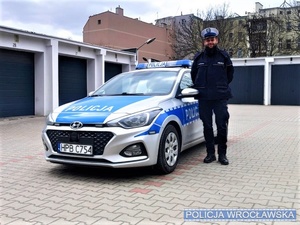 Umundurowany policjant stojący przy oznakowanym radiowozie