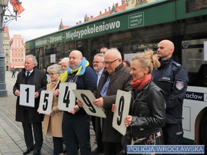 Uczestnicy stojący przed autobusem układający z tabliczek z cyframi liczbę 15499