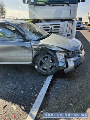 Zdjęcie zdarzenia drogowego, na którym widać, na pierwszym planie, auto osobowe oraz pojazd ciężarowy z widocznymi uszkodzeniami stojące na jezdni