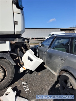 Zdjęcie zdarzenia drogowego, na którym widać, na pierwszym planie, auto osobowe oraz pojazd ciężarowy z widocznymi uszkodzeniami stojące na jezdni