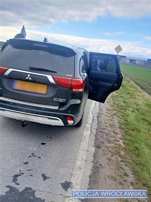 Stojący na jezdni widoczny od tyłu samochód osobowy marki mitsubishi z otwartymi drzwiami