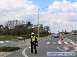 Stojący na drodze funkcjonariusz z ręcznym miernikiem prędkości w jednej ręce i tarczą do zatrzymywania pojazdów w drugiej