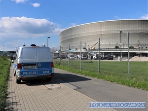 Stojący na tle stadionu oznakowany radiowóz policyjny