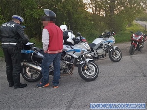 Policjant z zatrzymanym motocyklistą stojący przy policyjnym motocyklu