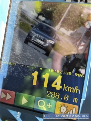 Zdjęcie wyświetlacza ręcznego miernika prędkości z zarejestrowanym przekroczeniem prędkości z widocznym pojazdem osobowym