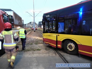 Stojący na jezdni uszkodzony w zdarzeniu drogowym autobus oraz strażak i pracownik nadzoru ruchu pomiędzy autobusem a wozem strażackim