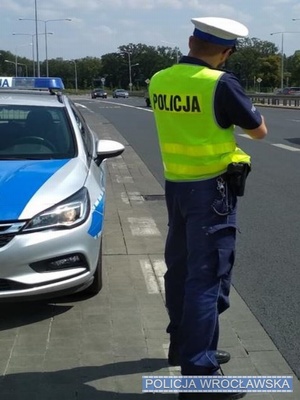 Zdjęcie umundurowanego policjanta ruchu drogowego stojącego obok oznakowanego radiowozu na jednej z wrocławskich ulic