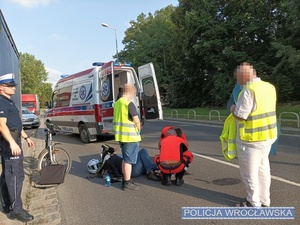 Ratownicy medyczni, umundurowany policjant i leżący na jezdni mężczyzna