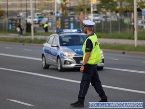 Policjant w mundurze na drodze  w tle policyjny radiowóz