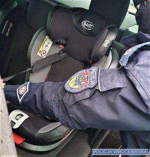 Umundurowany policjant montujący fotelik na tylnej kanapie auta - zdjęcie poglądowe