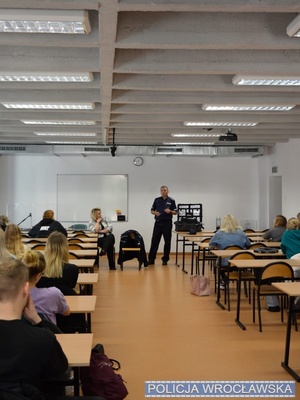 Sala wykładowa ze studentami oraz policjant w mundurze prowadzący zajęcia