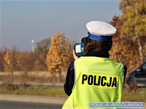 Umundurowana policjantka w trakcie wykonywania pomiaru prędkości przy użyciu ręcznego miernika prędkości - zdjęcie poglądowe