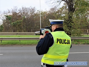 Umundurowany funkcjonariusz ruchu drogowego na jednej z wrocławskich ulic w trakcie wykonywania pomiaru prędkości