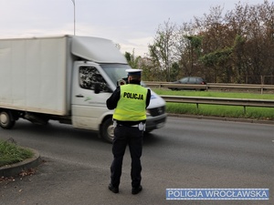 Umundurowany funkcjonariusz ruchu drogowego na jednej z wrocławskich ulic w trakcie wykonywania pomiaru prędkości