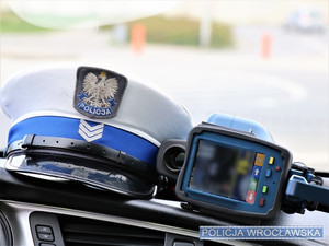 Zdjęcie poglądowe leżących na podszybiu auta czapki policjanta ruchu drogowego w stopniu sierżanta sztabowego oraz ręcznego miernika prędkości