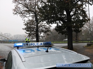 Dwaj umundurowani policjanci ruchu drogowego przy jednej z wrocławskich ulic, a na pierwszym planie oznakowany radiowóz Policji.