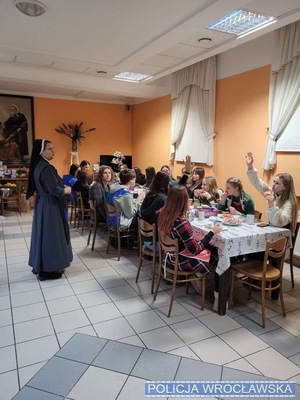 Uczniowie siedzący przy stole siostra zakonna stoi