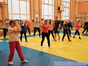 Grupa ludzi na sali gimnastycznej trenuje zajęcia sporotwe