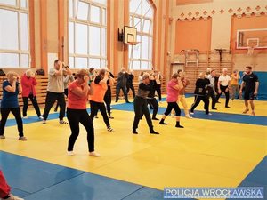 Grupa ludzi na sali gimnastycznej trenuje zajęcia sporotwe