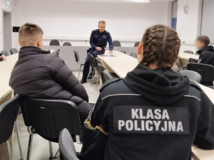 Zdjęcie siedzących w sali przed umundurowanym policjantem uczniów