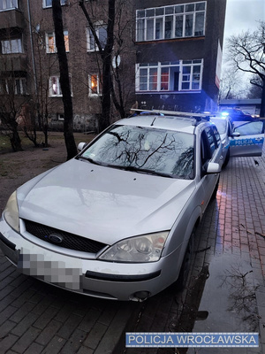 Stojący przy jednej z wrocławskich ulic osobowy ford, za którym stoi oznakowany radiowóz Policji