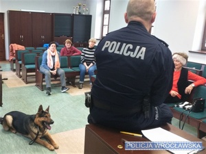 Umundurowani policjanci wraz z psem służbowym podczas spotkania ze słuchaczami Uniwersytetu Trzeciego Wieku na Uniwersytecie Wrocławskim