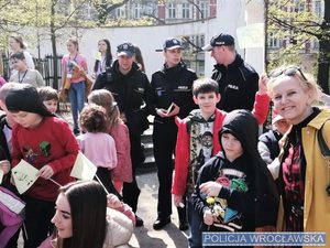 Grupa dzieci, kobieta oraz policjanci w mundurze w tle