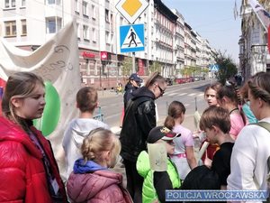 Grupa młodzieży z policjantką w mundurze w tle oraz dorosłym opiekunem