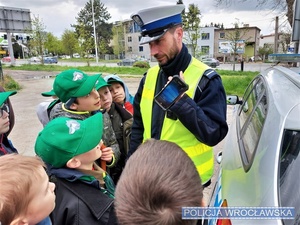 Zdjęcie zuchów wraz z umundurowanym policjantem stojącymi przy oznakowanym radiowozie