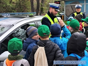 Zdjęcie zuchów wraz z umundurowanymi policjantami stojącymi na placu przy oznakowanym radiowozie