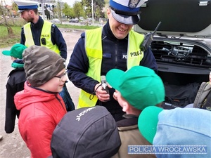 Zdjęcie zuchów wraz z umundurowanymi policjantami stojącymi przy oznakowanym radiowozie