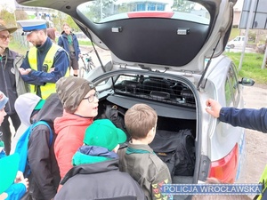 Zdjęcie zuchów wraz z umundurowanym policjantem stojącymi na placu przy oznakowanym radiowozie