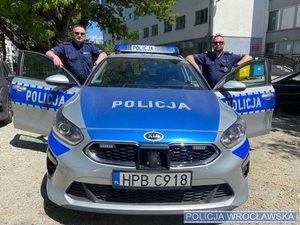 Policjanci w mundurze stojący przy radiowozie w tle komisariat policji Wrocław Stare -Miasto