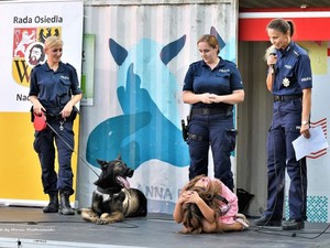 Policjantki w mundurach służbowych na scenie wraz z sem służbowym, Dziewczynka demonstrująca postawę jaką należy przyjąć przy ataku przez psa.