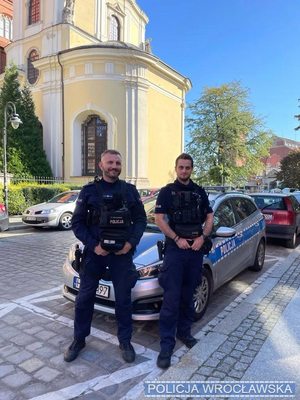 Policjanci w mundurach na tle policyjnego radiowozu