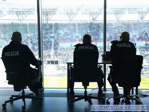 Policjanci w mundurach siedzący tyłem w pomieszczeniu stadionu miejskiego w tle widok na murawę