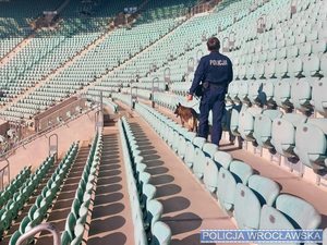 Policjant w mundurze z policyjnym psem służbowym sprawdza trybuny stadionu