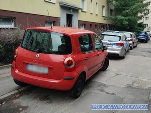 Zaparkowane na jednej z wrocławskich ulic osobowe renault, przed którym stoi oznakowany radiowóz Policji