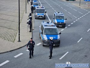 Zdjęcie umundurowanych funkcjonariuszy prewencji oraz oznakowanych radiowozów na parkingu przy stadionie miejskim we Wrocławiu.